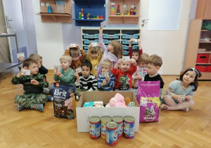 Dzieci siedzą na podłodze prezentując zebrane przez przedszkole darów dla zwierzaków z fundacji tymmmczasy.
